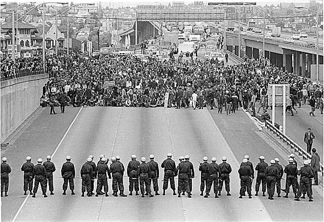 May 5, 1970: Thousands of University of Washington students occupying and blocking Intersate Highway 5 (I-5) and facing state troopers in riot gear as they protested the killings at Kent State Universtiy and the invasion of Cambodia. Photo, Museum of History & Industry, Seattle.