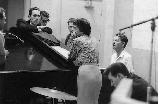 Early 1960s: RCA studio session of Nashville musicians, from left: Bob Moore, Chet Atkins (arms folded on piano), Louis Nunley, Gil Wright, Anita Kerr (leaning on piano, back to camera), Willie Ackerman, and Floyd Cramer.