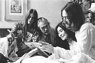 June 1969: Rosemary & Timothy Leary, Yoko Ono, and John Lennon, reading newspaper story about their “Bed-In” peace demonstration. Photo, Stephen Sammons