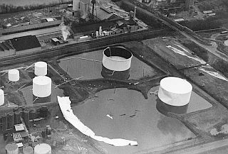 Aerial photo looking down on the scene with twisted shell of split tank remaining and “dented” neighboring tank at right.