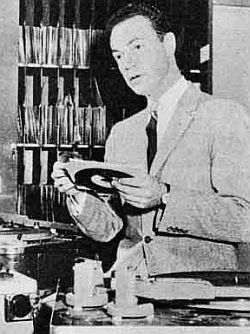 Disc jockey Alan Freed shown in studio with 45 rpm recording in hand to play on his show.