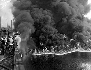 1952: Photo from an earlier Cuyahoga River fire, caused by the river’s severe pollution, shows firemen on railroad bridge at left battling the blaze on the river below.