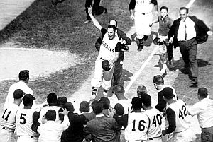 Bill Mazeroski, on final leg of home run trot, is pursued by fans as he makes his way to home plate where his teammates await. Has become iconic photo; click for autographed 8x10 copy.