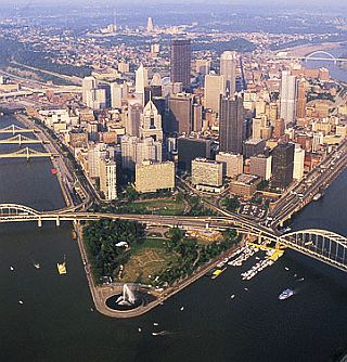 Pittsburgh in more recent times at the juncture of the Allegheny & Monongahela Rivers, with Cathedral of Learning visible in the far distance, top center, marking former location of Forbes Field.