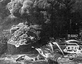 Boiling fire on top of large tank at left, with twisted metal thrown from explosion in the foreground. Whiting refinery fire, Aug 1955.