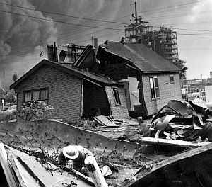 Part of the destruction from the 1955 Whiting oil refinery explosion & fire. Investigative worker in foreground is inside large piece of structural metal thrown there from explosion.