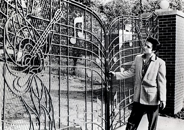 1957: Elvis Presley stands at the wrought iron gates he had made for the entrance drive at Graceland,  made to resemble a page of sheet music with musical notes and guitar players depicted. 