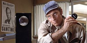 Unhappy detective Robert Thorn at police headquarters where a “Re-Elect Governor Santini” poster is visible.